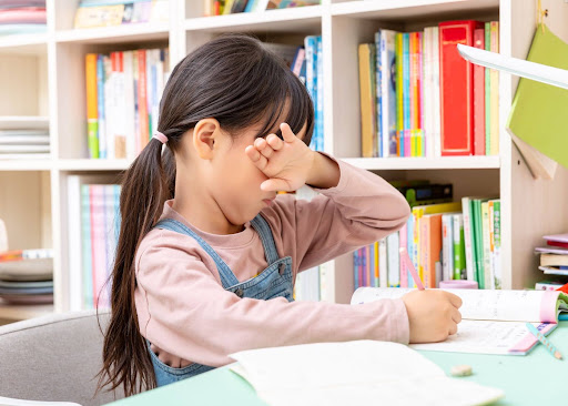 Child rubbing her eye while doing schoolwork, a possible sign of a vision problem